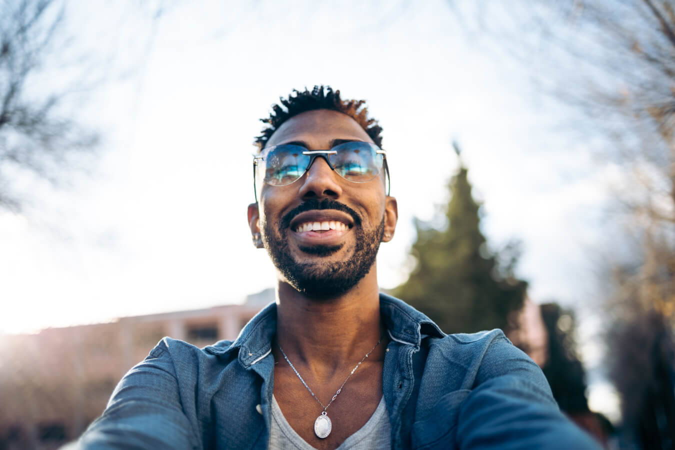 Handsome african american man with glasses taking a selfie with his smartphone in the street (looking at camera)